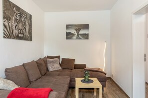 Un salon avec un canapé marron, une petite table en bois et deux œuvres d’art accrochées au mur.