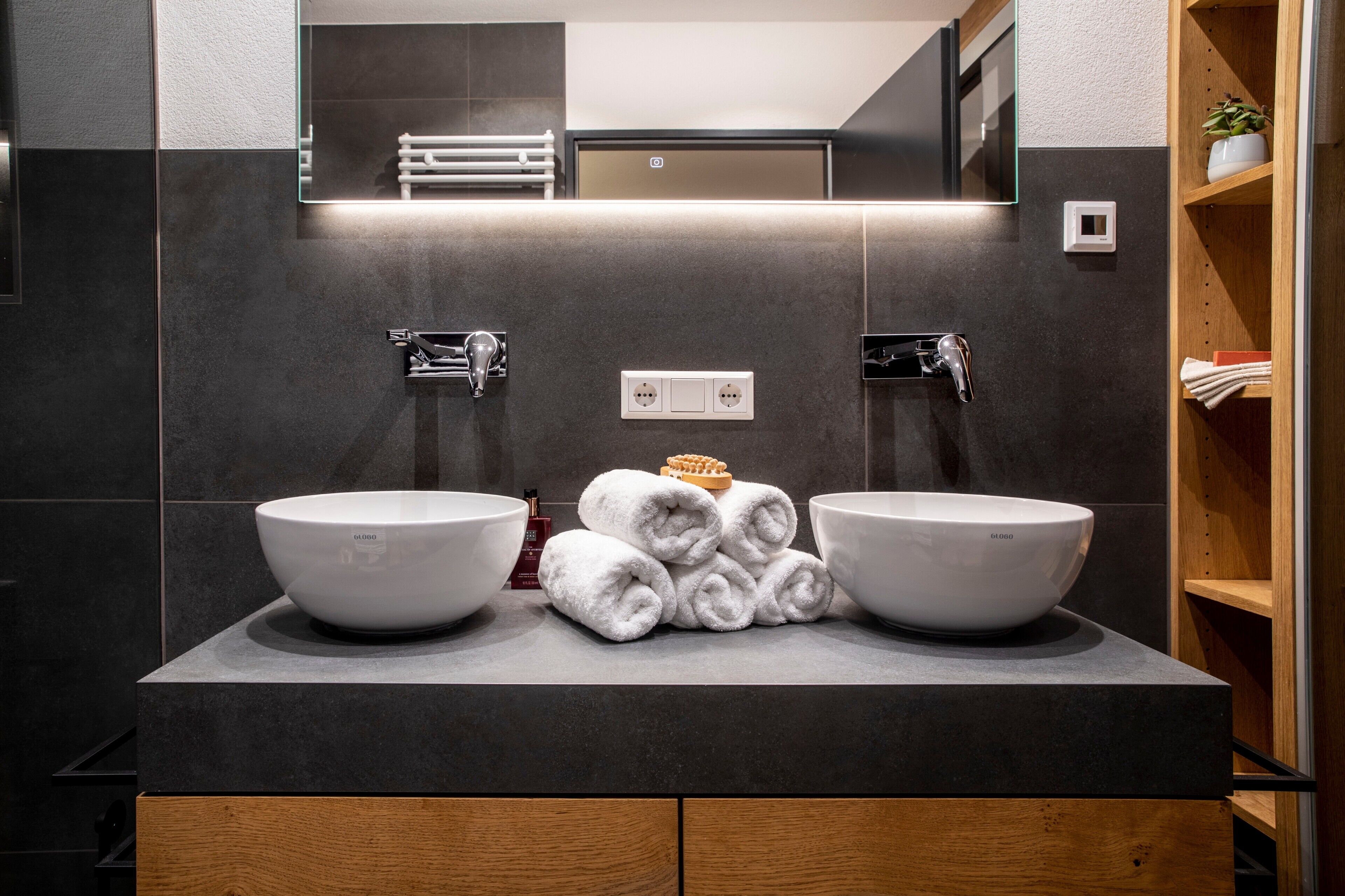A modern bathroom with two large white sinks, a mirror above, and a towel stack in the center.