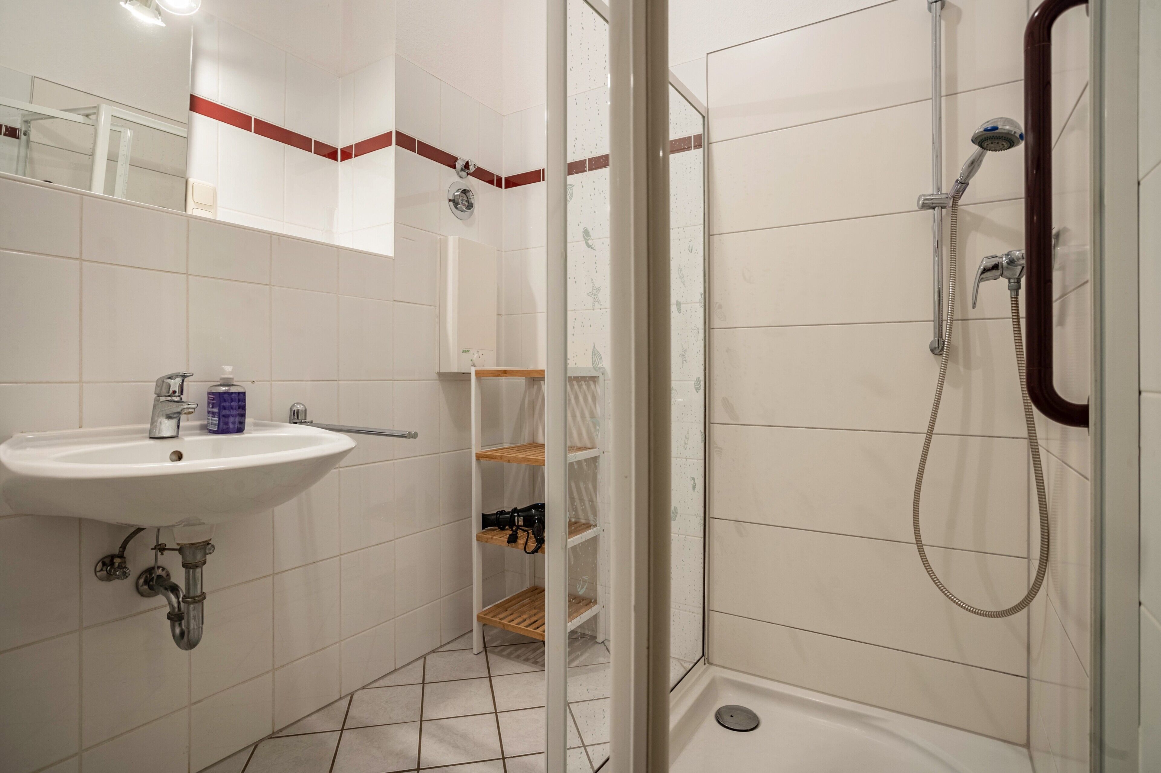 A bathroom with a sink, mirror, shower, and shelves.