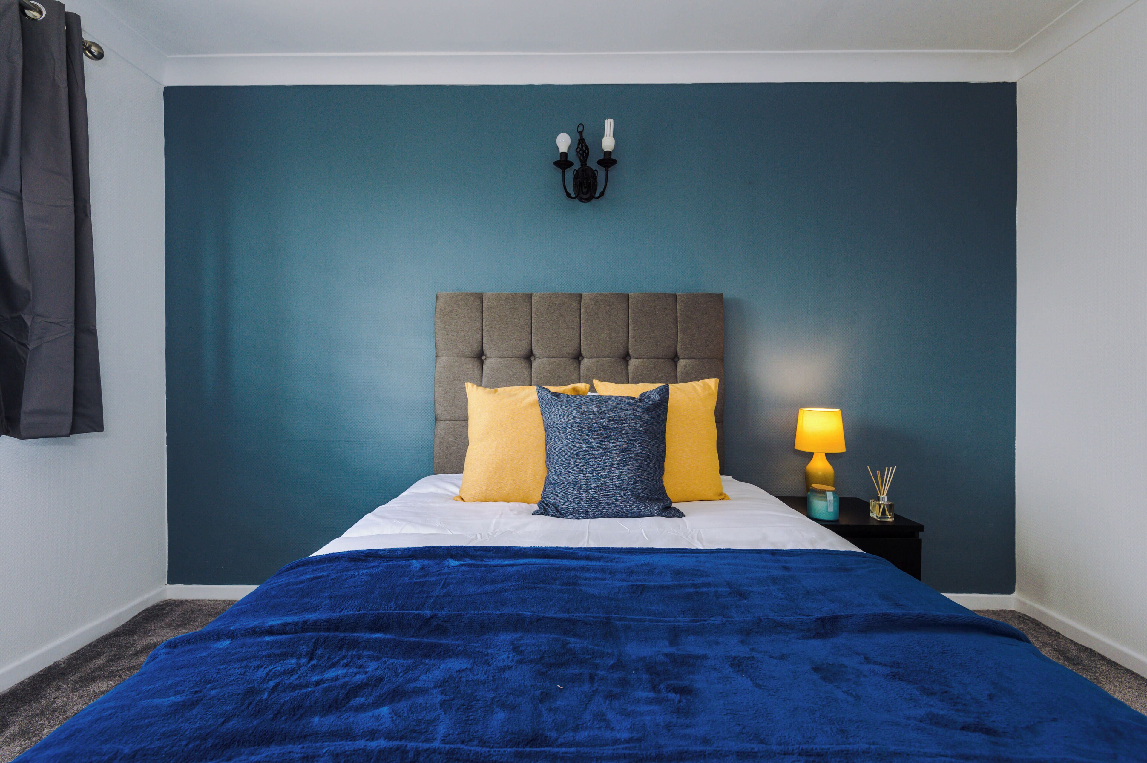 A bedroom with a tufted headboard, a blue bedspread, and two pillows.