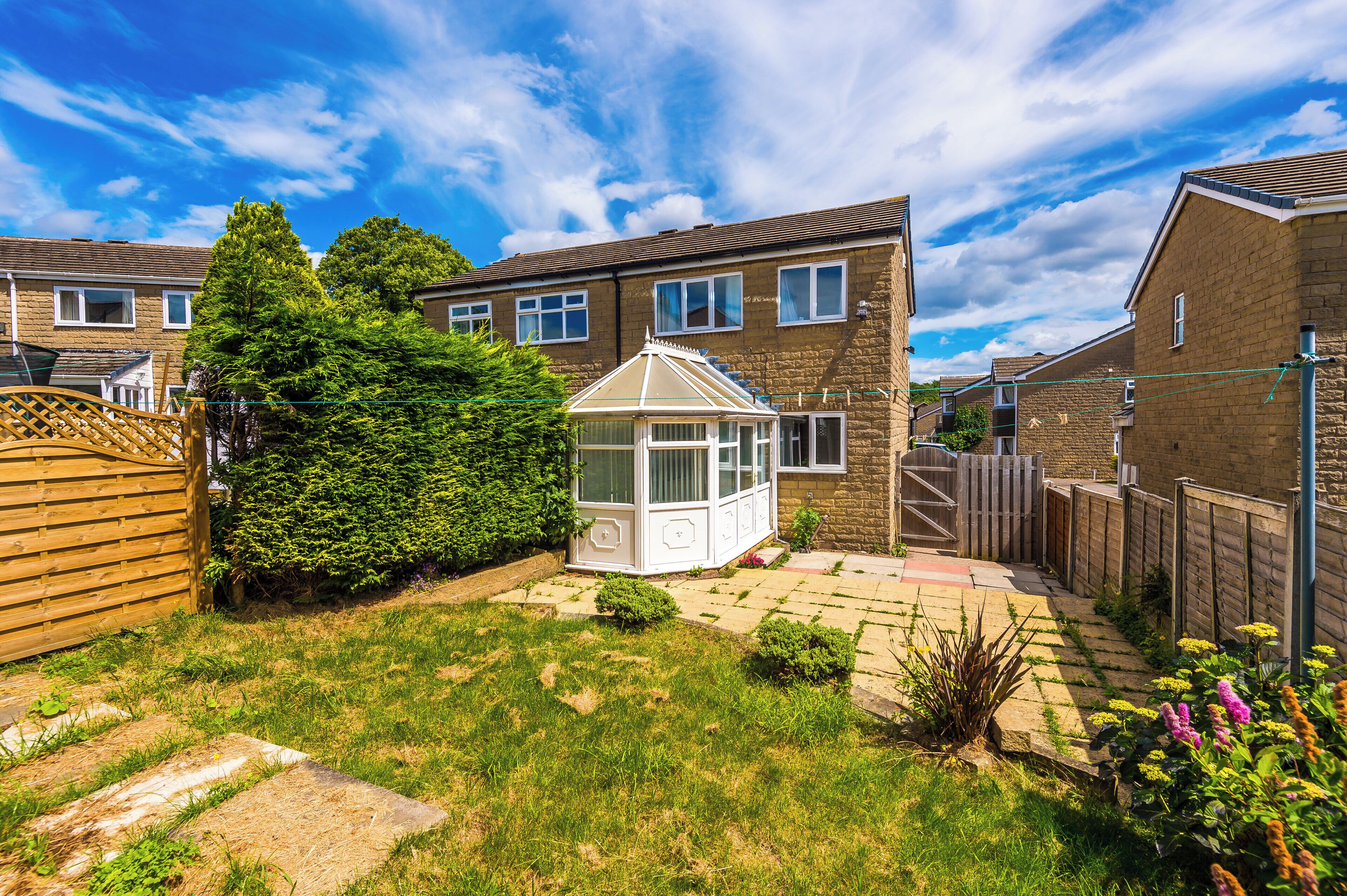 A residential backyard with a conservatory, a wooden fence, and a brick house.