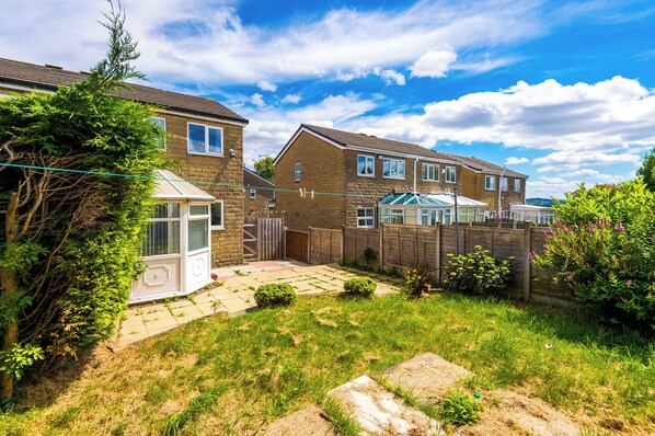 A residential backyard with a conservatory, a paved patio, and a wooden fence.
