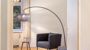 Een moderne kamer met een donkergrijze fauteuil, een glazen tafel, een vloerlamp en uitzicht door een raam.
