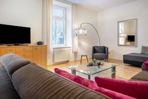 A modern living room with a flat-screen TV, a glass coffee table, a grey sofa, a grey armchair, and a large mirror. - Apartment 'Parkblick' with Shared Garden and Wi-Fi (Groß Plasten)