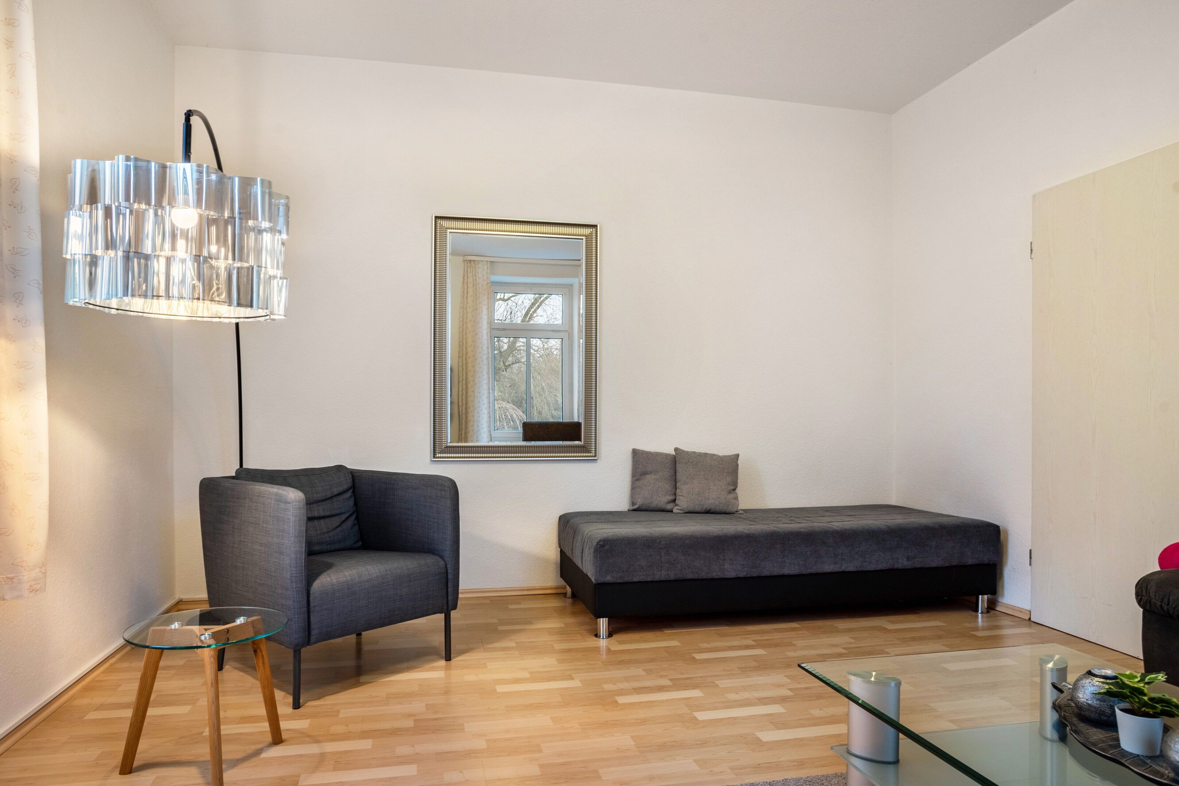 A modern bedroom with a bed, a chair, a glass table, and a floor lamp.