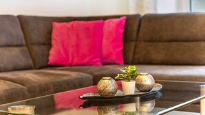 Een woonkamer met een bruine bank, een roze kussen en een glazen salontafel met decoratieve objecten.