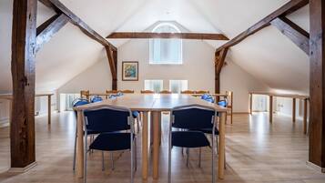 A large room with a high ceiling, wooden beams, and a long table with chairs.