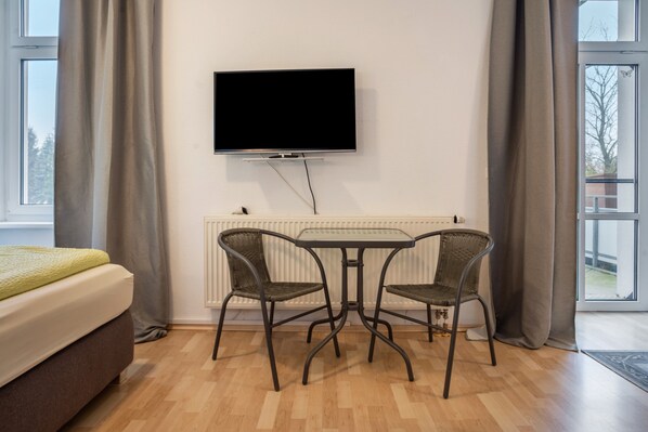 Una habitación con una cama, un televisor en la pared y dos sillas alrededor de una pequeña mesa.