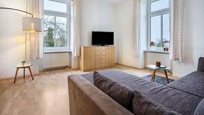 Ett modernt vardagsrum med en soffa, en tv på ett träskåp, en lampa och ett litet bord med en kopp på.