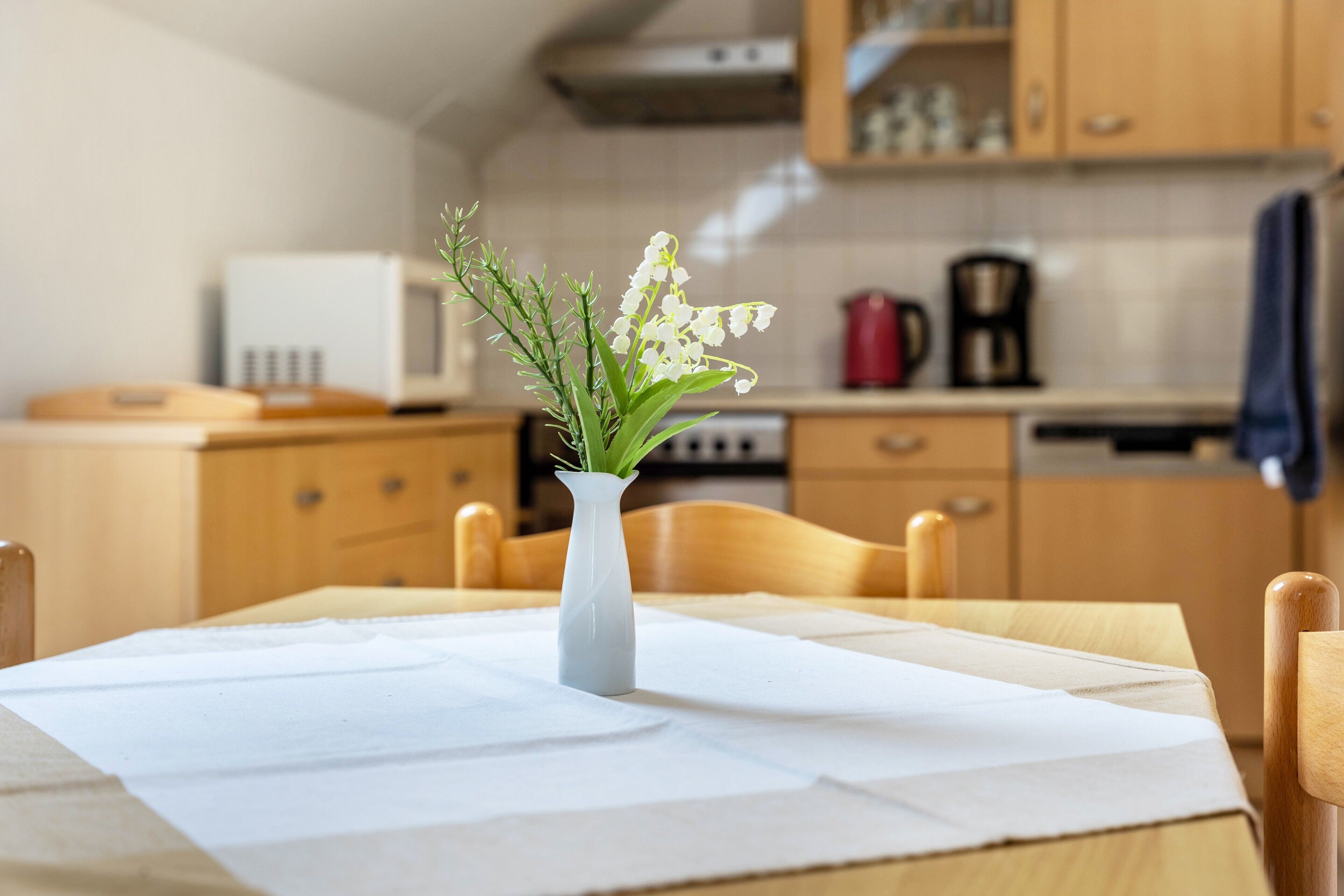 A dining table with a white tablecloth, a white vase with flowers, and wooden chairs.
