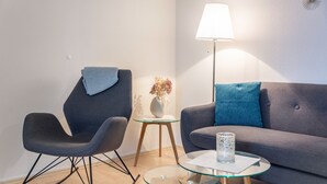 Ein modernes Wohnzimmer mit einem grauen Sofa, einem Schaukelstuhl, einem Glastisch, einer Stehlampe und einer Vase mit getrockneten Blumen.