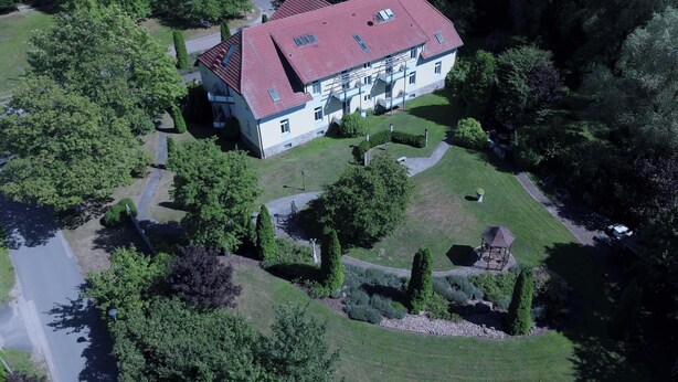Ein Luftbild eines großen, zweistöckigen Gebäudes mit rotem Dach, umgeben von üppiger Vegetation und einem gepflegten Garten.
