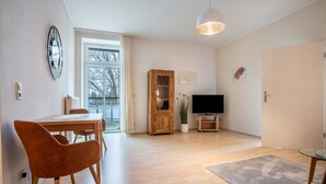 Ein modernes Wohnzimmer mit einem Holzesstisch, einer Couch, einem Fernseher und einem großen Fenster.