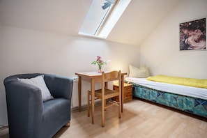 A small room with a sloped ceiling, a desk, a chair, a sofa, a bed, and a window.