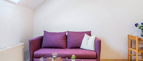 Et værelse med en lilla sofa, et glasbord med en plante og en træstol.