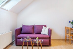 Une pièce avec un canapé violet, une table en verre ornée d’une plante et une chaise en bois.