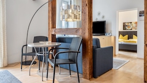 A modern living room with a round table, two chairs, a sofa, a television, and a wooden beam structure.