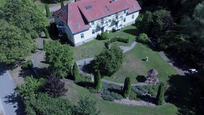 An aerial view of a large, two-story building with a red roof, surrounded by lush greenery and a well-maintained garden.
