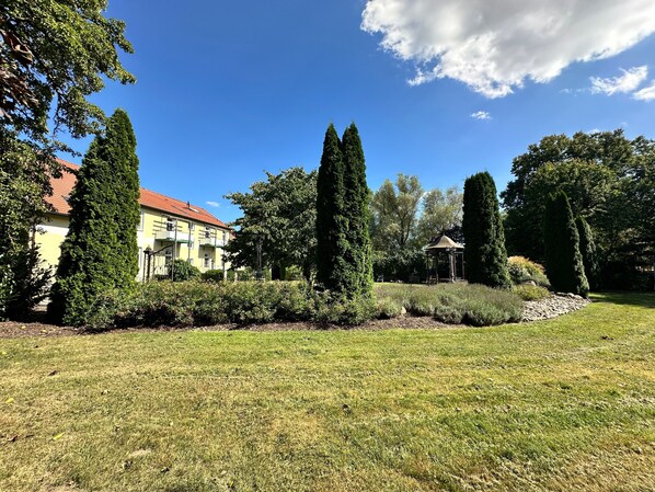 A residential area with a well-maintained lawn, a gazebo, and a building with a red roof.