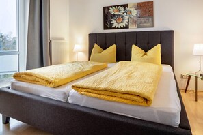 Una cama doble con cabecera oscura, dos almohadas y una manta amarilla.