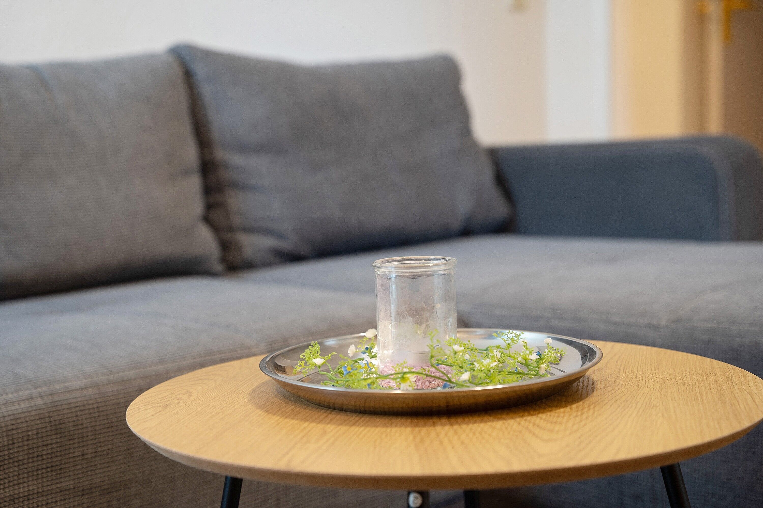 Une table ronde en bois, sur laquelle se trouvent un porte-bougie en verre et un plateau en métal décoré de fleurs.