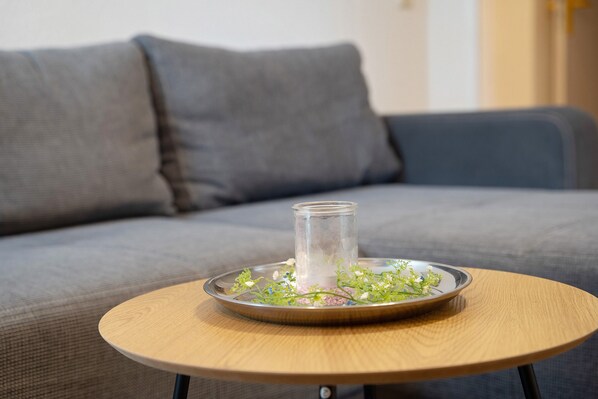 A round wooden table with a glass candle holder and a metal tray with flowers.