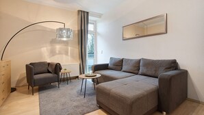 Una sala de estar moderna con un sofá, un sillón, una mesita, una lámpara de pie y un espejo en la pared.