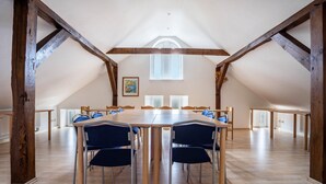 Una habitación amplia con techo alto, vigas de madera y una larga mesa con sillas.