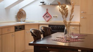 Una cocina moderna con una mesa de madera, sillas, un jarrón con plantas secas y una toalla de cocina roja en la pared.