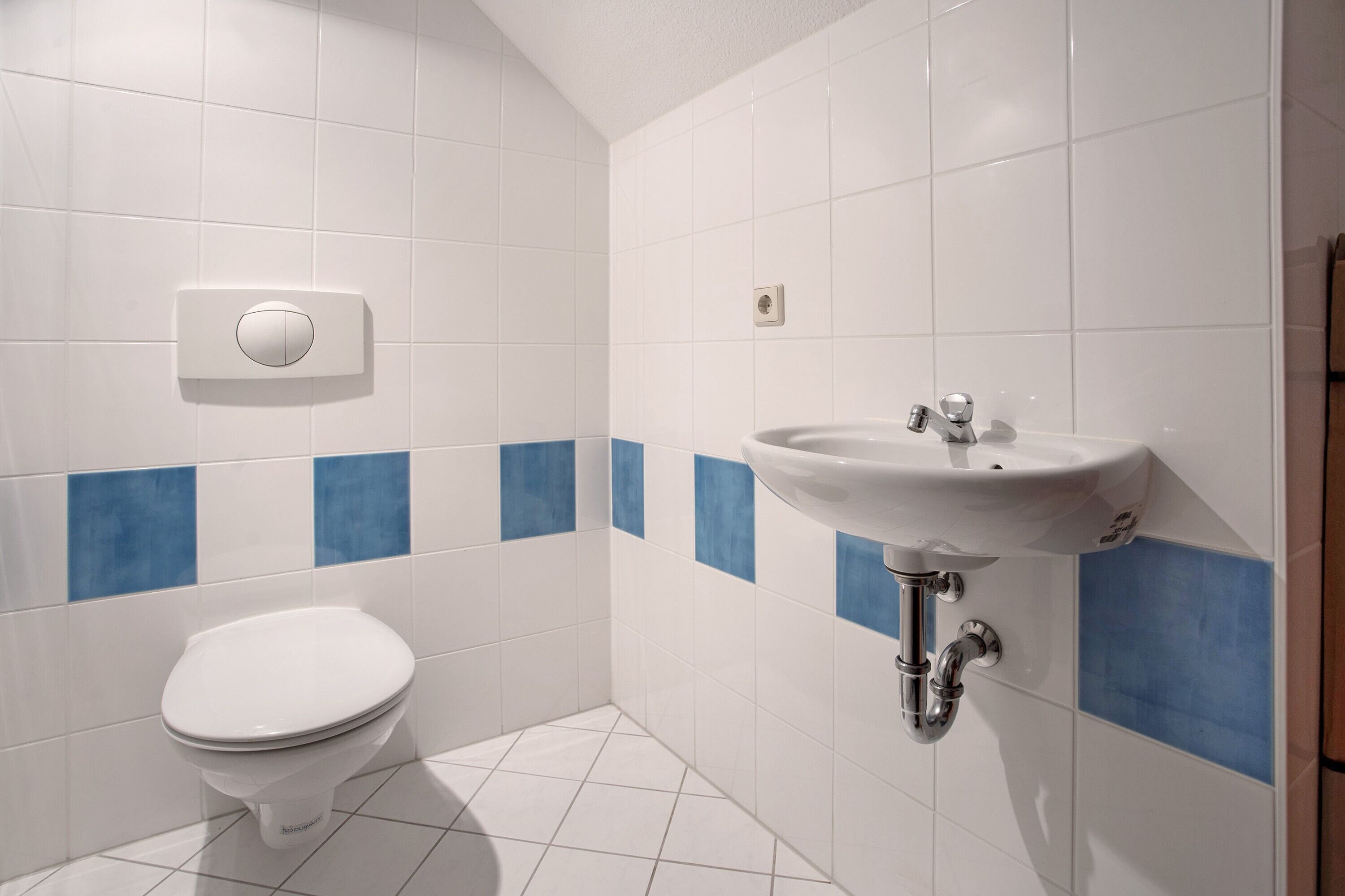 Ein Badezimmer mit Toilette, Waschbecken und ein an der Wand montiertem Thermostat.