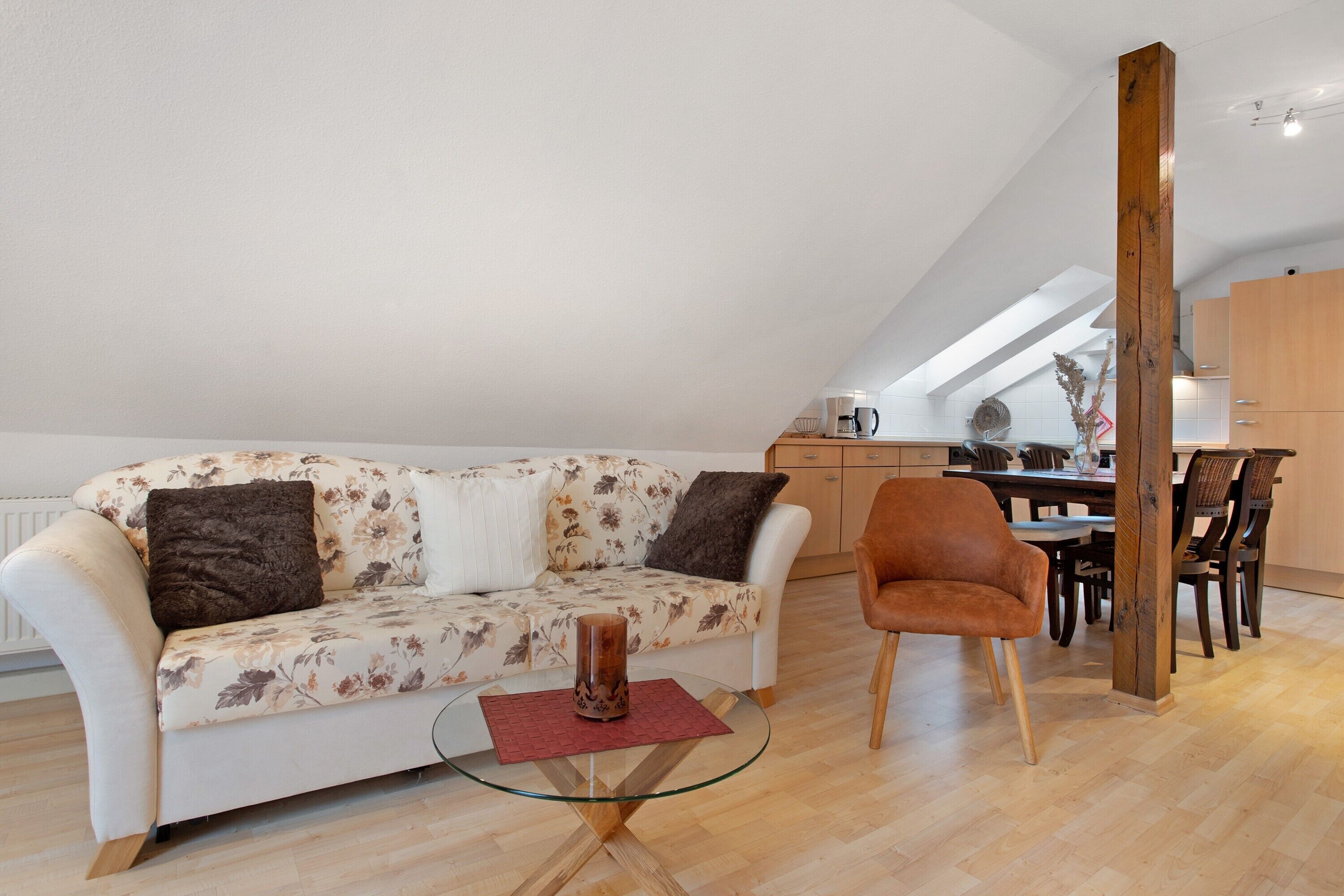 Ein modernes Loft mit hoher Decke, einem weißen Sofa mit floralem Bezug, einem Glastisch und einem Essbereich mit Holztischen und Stühlen.