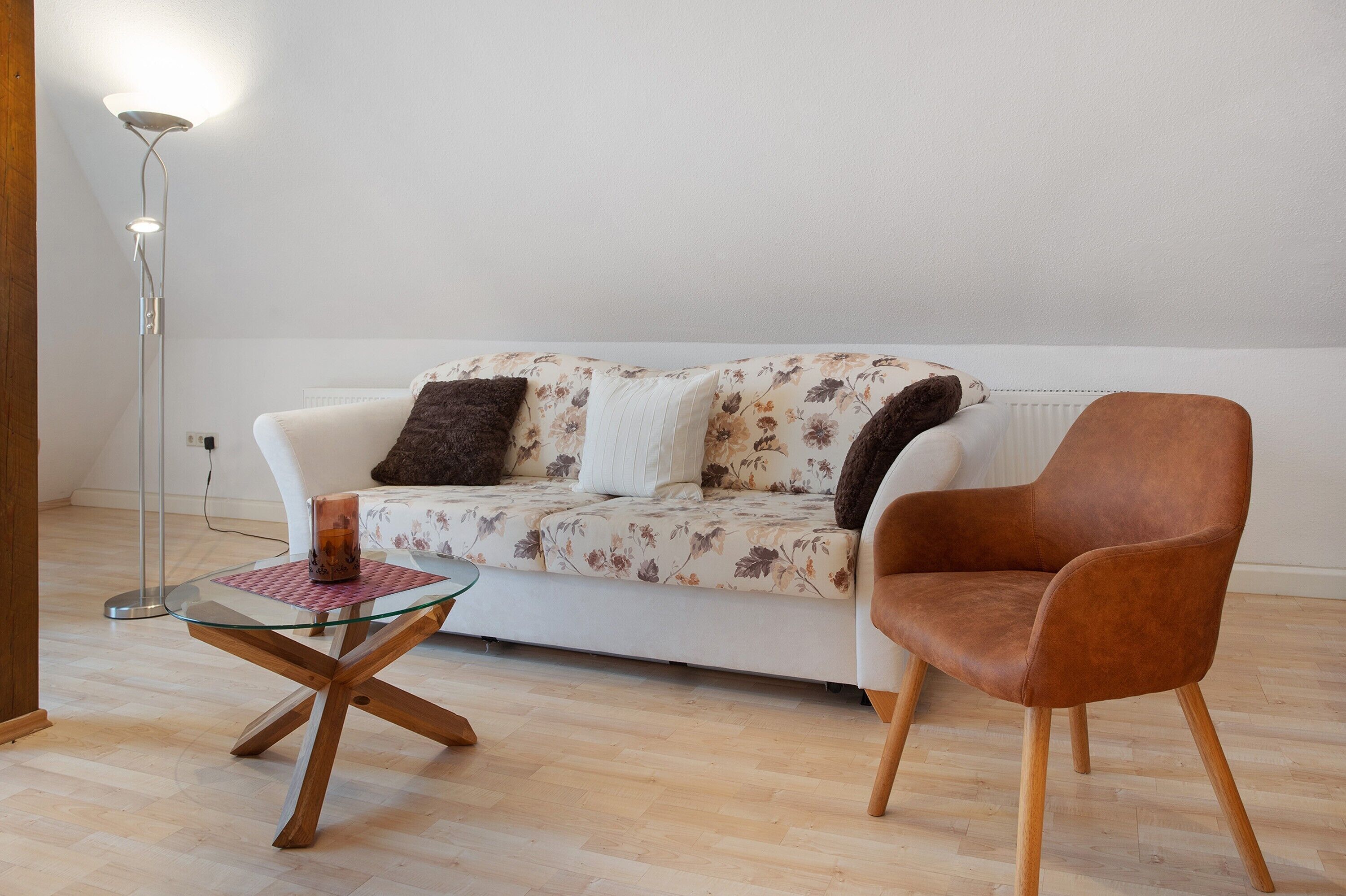 A living room with a sofa, a glass coffee table, a brown armchair, and a floor lamp.
