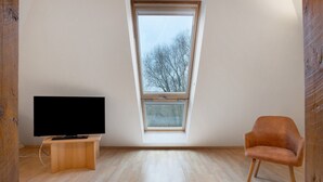 Una habitación con una televisión sobre un soporte de madera, una ventana con vistas a árboles y un suelo de madera.