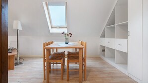 Een kamer met een eettafel, stoelen, een vaas met bloemen, een lamp en een witte wandplank.