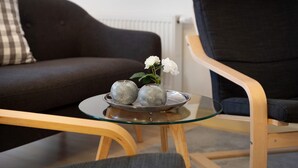 Een moderne woonkamer met een glazen salontafel, een donkere bank en een houten stoel.