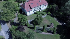 Luchtbeeld van een groot, tweelaags gebouw met een rood dak, omgeven door weelderige begroeiing en een verzorgde tuin.