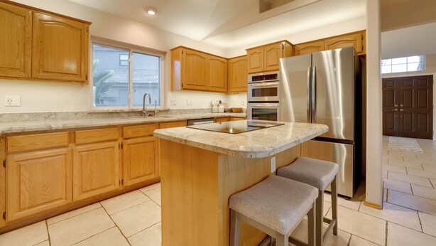A modern kitchen with wooden cabinets, a stainless steel refrigerator, and a bar area with stools. - Home on Golf Course w/ Private Pool in Phoenix! (Phoenix)