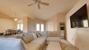 A living room with a sectional sofa, a coffee table, a flat-screen TV, and a ceiling fan. - Home on Golf Course w/ Private Pool in Phoenix! (Phoenix)
