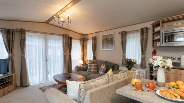 A cozy living room with a sofa, coffee table, and a dining area with a table set for breakfast. - Cairn View by Interhome (Aviemore)