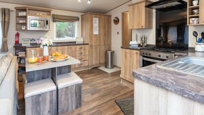 A compact kitchen with wooden cabinets, a stove, and a sink. There is a small seating area with stools and a window providing natural light. - Cairn View by Interhome (Aviemore)