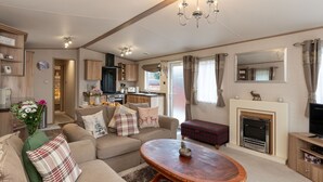 A cozy living room with a sofa, a coffee table, and a fireplace. There is a kitchen area with cabinets and a stove. - Cairn View by Interhome (Aviemore)