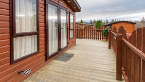 A wooden cabin with large windows, a wooden deck, and a fenced area. - Cairn View by Interhome (Aviemore)