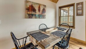 Un comedor con una mesa de madera, sillas negras y un cuadro de árboles en la pared.