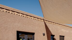 Une façade d’immeuble avec un revêtement extérieur en stuc texturé, une fenêtre dotée d’un cadre foncé et un petit luminaire fixé au mur.