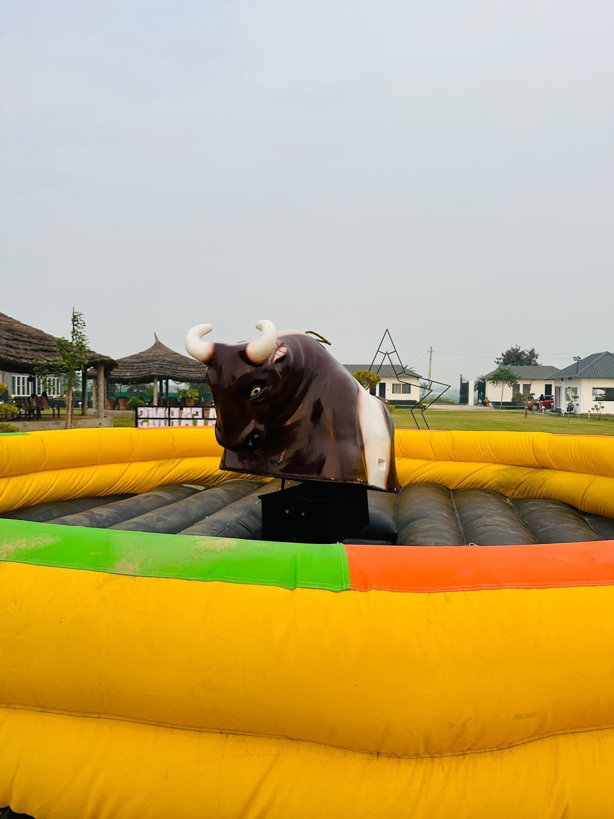 An inflatable bull ride with a yellow and green base, set in an outdoor area with buildings in the background.