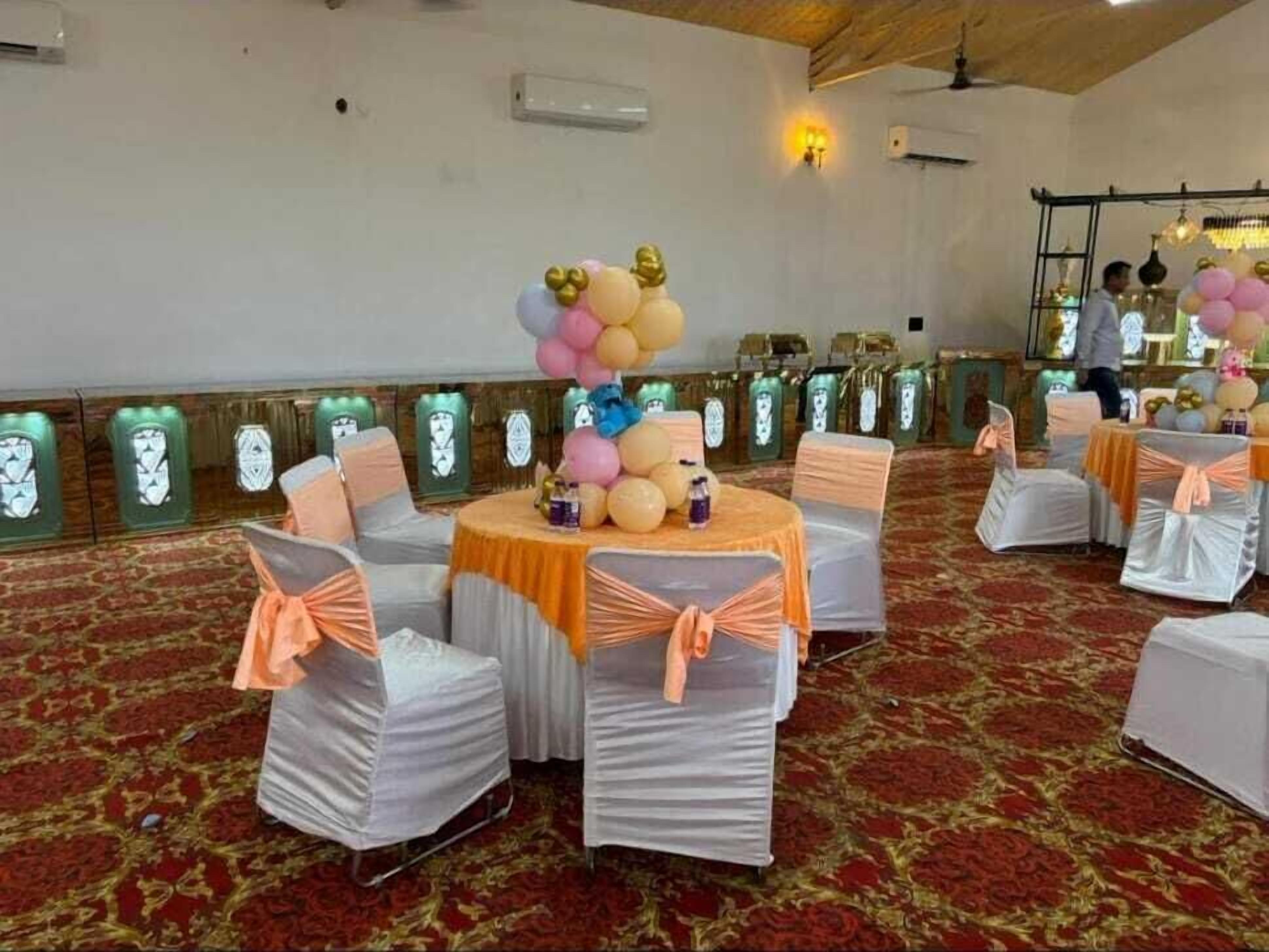 A banquet hall with round tables covered in orange tablecloths, surrounded by white chairs with orange sashes.