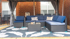 A covered patio area with wicker furniture, a small table, and a sign welcoming guests to the porch.