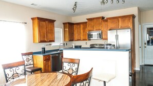 A kitchen with wooden cabinets, a central island, a dining table with chairs, and a refrigerator.