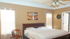 A bedroom with a bed, a ceiling fan, a wall clock, and a window with blinds.
