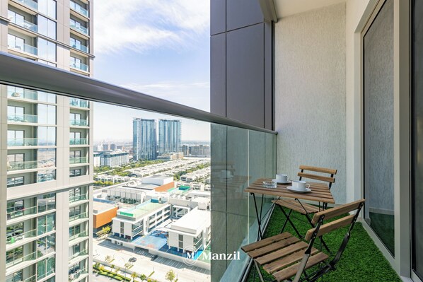 A balcony with a table and chairs, a view of a cityscape, and a building with balconies.